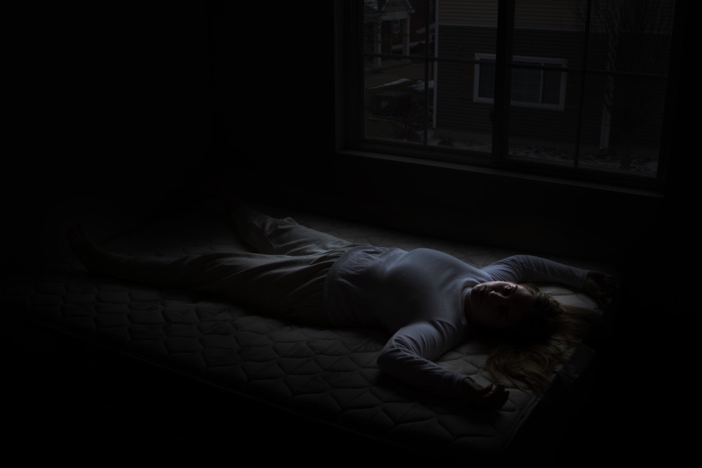 Very dark photo of a young woman barely visible lying on her back looking up at the camera.